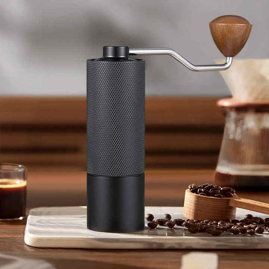 Black manual coffee grinder with adjustable ceramic burrs on a wooden setting, ideal for fresh coffee grinding.